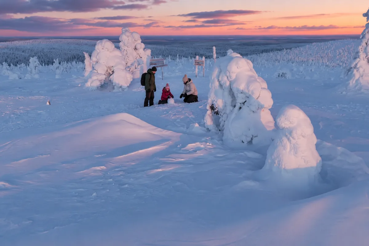 Persone tra gli alberi coperti di neve e ghiaccio su un altopiano della Lapponia al crepuscolo, con la foresta all’orizzonte