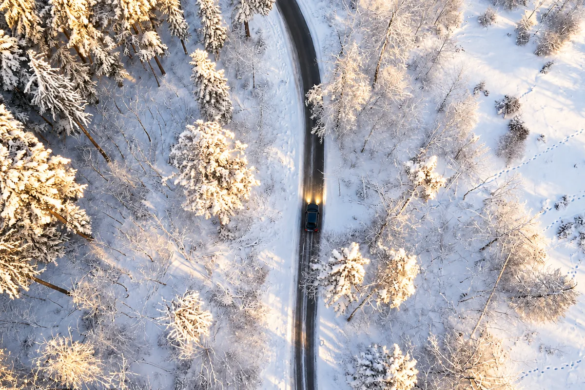 Veduta aerea di una strada stretta che attraversa una foresta innevata della Lapponia, con pini carichi di neve e un’auto in transito