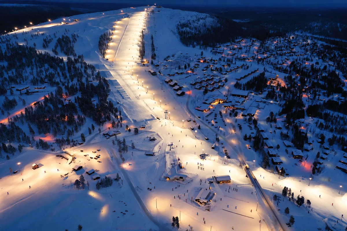 Piste da sci illuminate di notte tra la neve a Levi, in Lapponia, con gli edifici del resort ai piedi del pendio