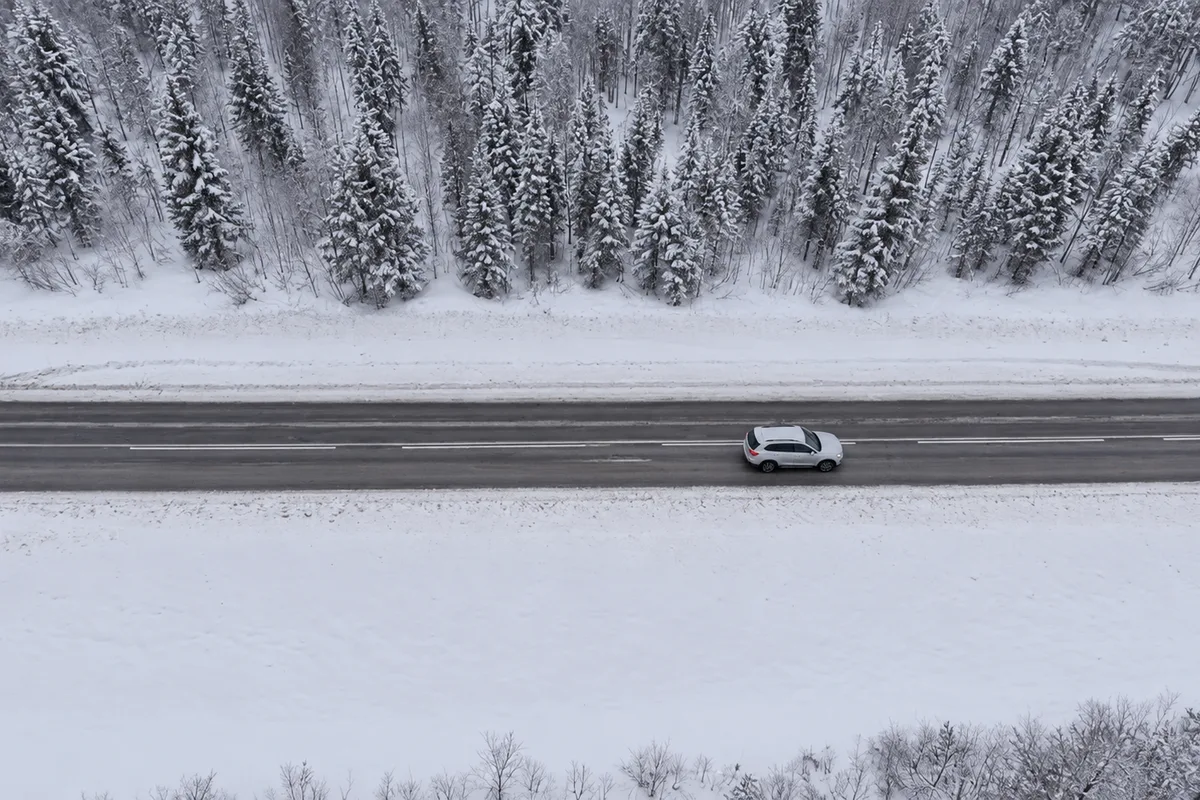 Vista dall’alto di un’auto su una strada innevata della Lapponia, con la foresta di pini coperta di neve ai lati