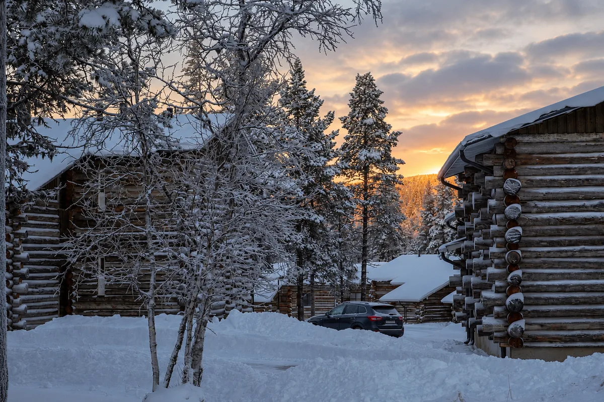 Case in tronchi innevate di un villaggio lappone tra betulle e abeti carichi di neve, al tramonto invernale