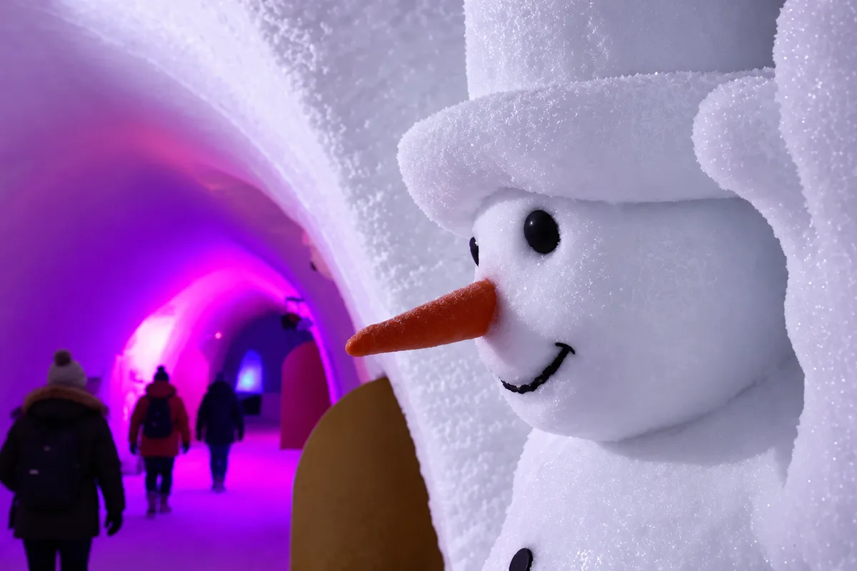 Pupazzo di neve scolpito in un tunnel di ghiaccio illuminato di viola al Snowman World di Rovaniemi, con visitatori sullo sfondo