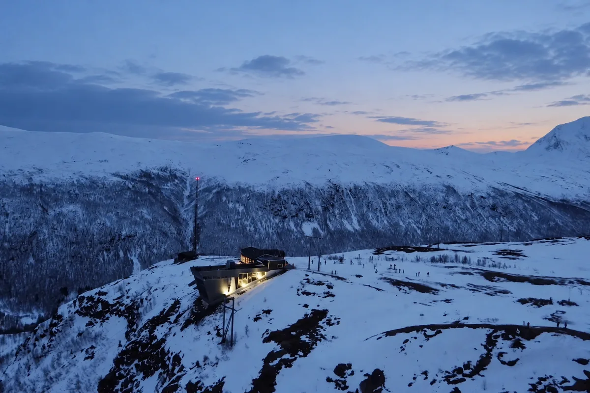 Veduta aerea del monte Storsteinen innevato sopra Tromsø, con la stazione della funivia illuminata al crepuscolo blu