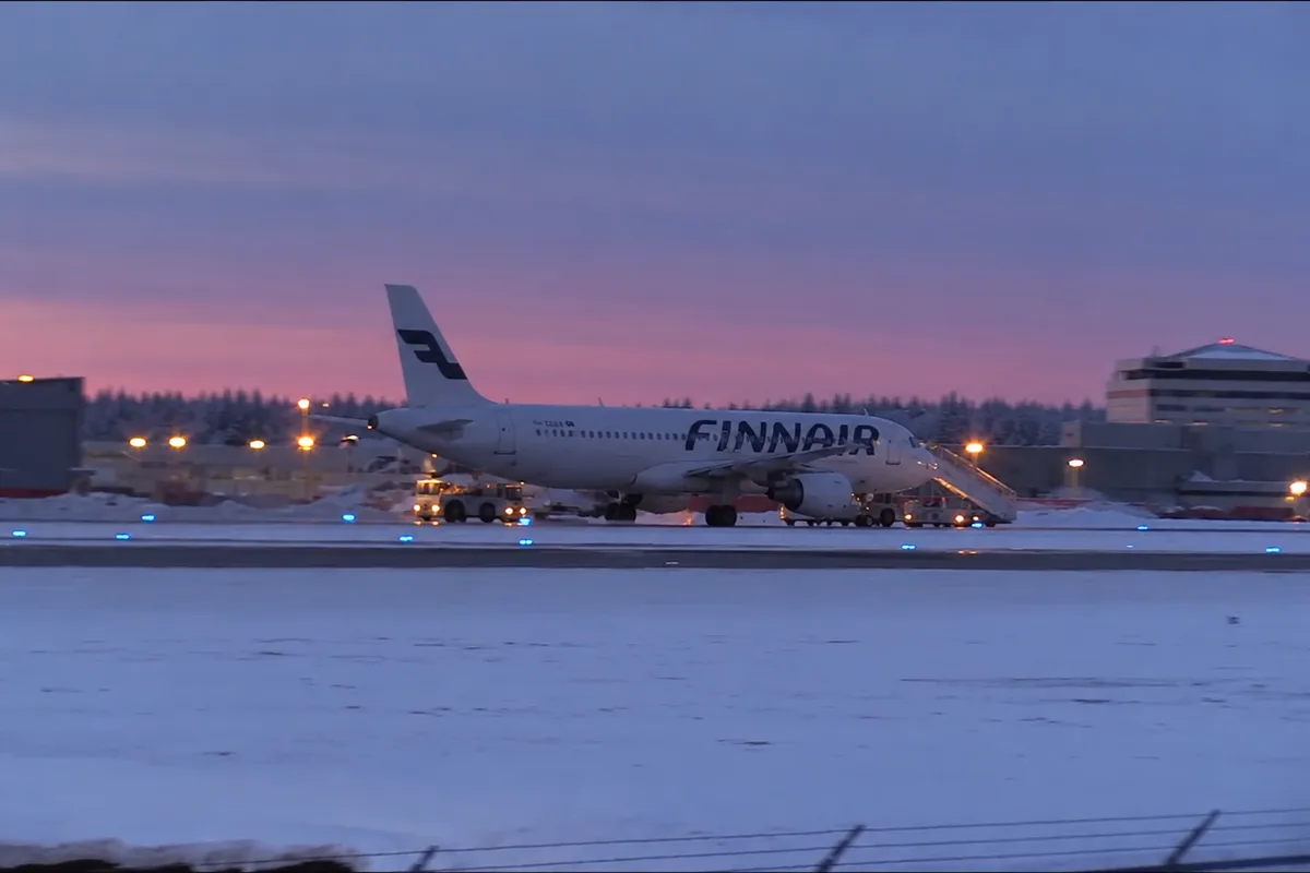 Aereo di linea sulla pista innevata dell’aeroporto di Rovaniemi al crepuscolo, con il terminal e le luci della pista